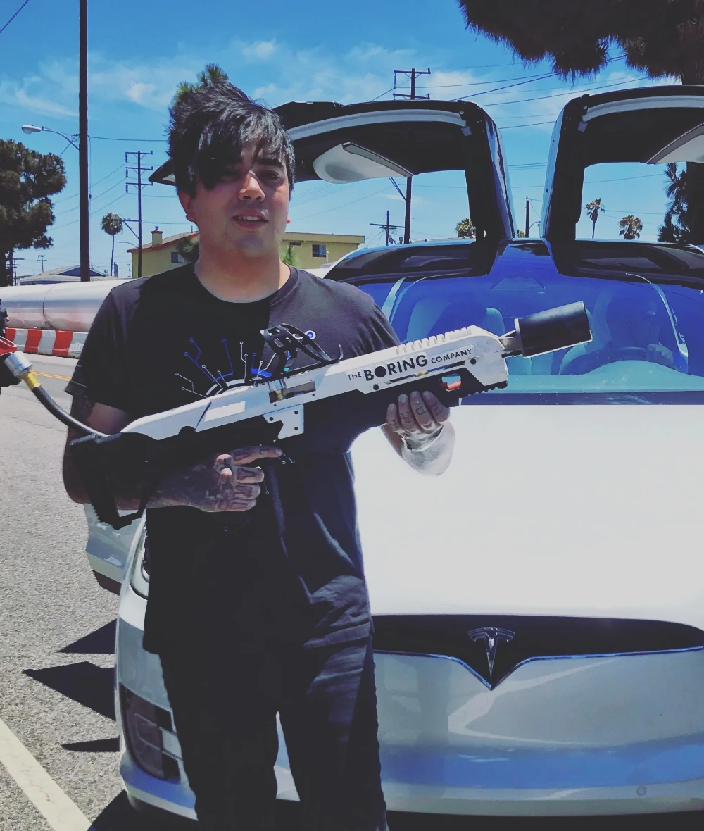 Eros Marcello holding a Boring Company device beside a Tesla Model X with its doors raised